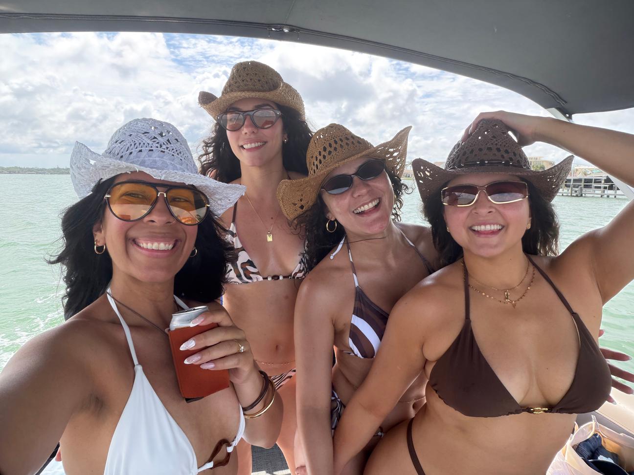 Four friends in sun hats laughing together aboard an Agua Blu charter on the water