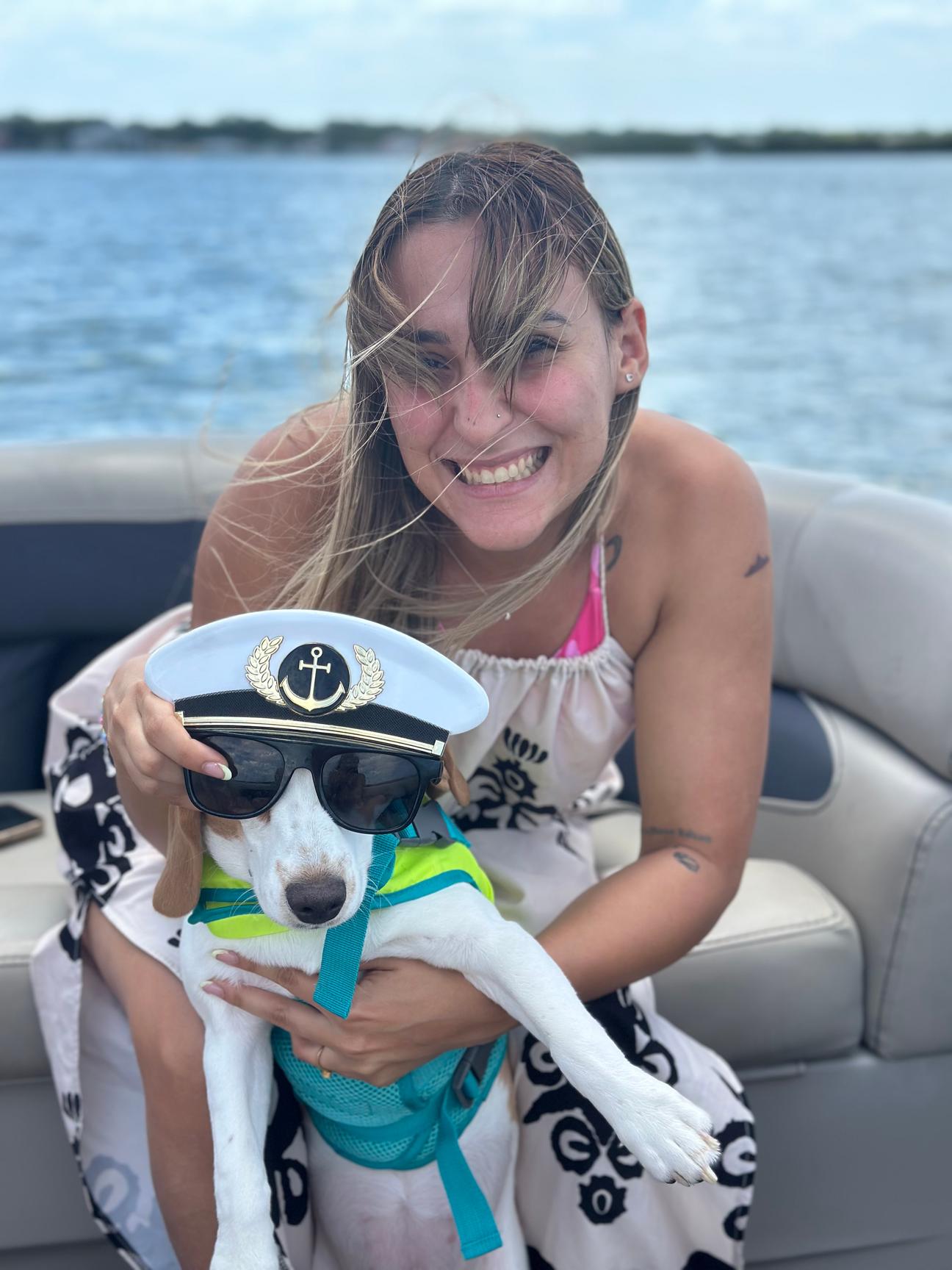 A guest holding her small dog wearing a captain's hat and sunglasses aboard the charter boat